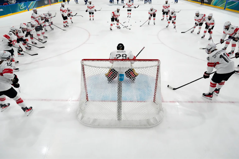 Hockey players in white and red jerseys in a semicircle around a goaltender seen from behind