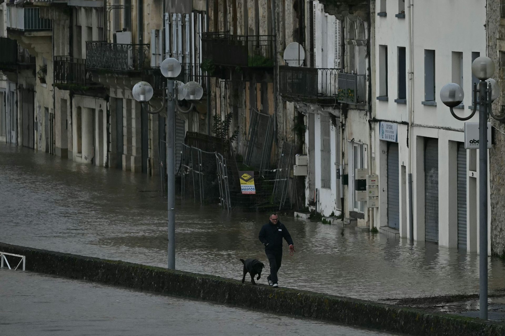 Un piéton promène son chien dans une rue inondée alors que les eaux de la Garonne en crue submergent les rues de La Réole, dans le sud-ouest de la France, le 12 février 2026, lors de la tempête Nils qui a provoqué des inondations dans toute la région.
