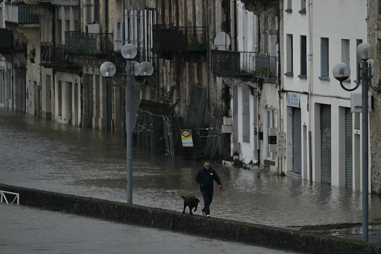 Un piéton promène son chien dans une rue inondée alors que les eaux de la Garonne en crue submergent les rues de La Réole, dans le sud-ouest de la France, le 12 février 2026, lors de la tempête Nils qui a provoqué des inondations dans toute la région.
