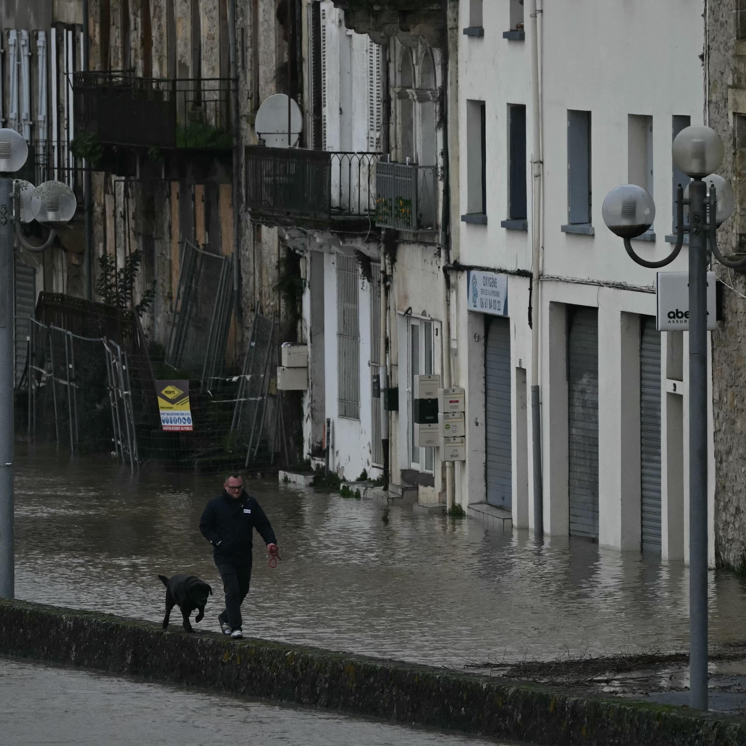 Un piéton promène son chien dans une rue inondée alors que les eaux de la Garonne en crue submergent les rues de La Réole, dans le sud-ouest de la France, le 12 février 2026, lors de la tempête Nils qui a provoqué des inondations dans toute la région.