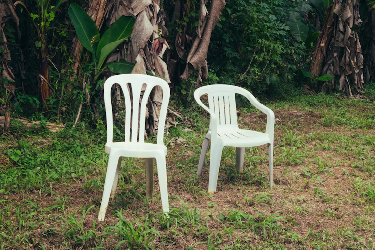 Dos sillas blancas de plástico en medio de un paisaje verde.