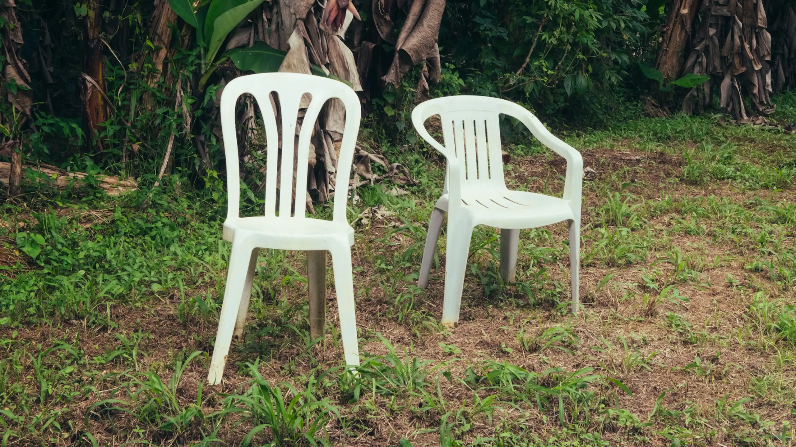 Dos sillas blancas de plástico en medio de un paisaje verde.