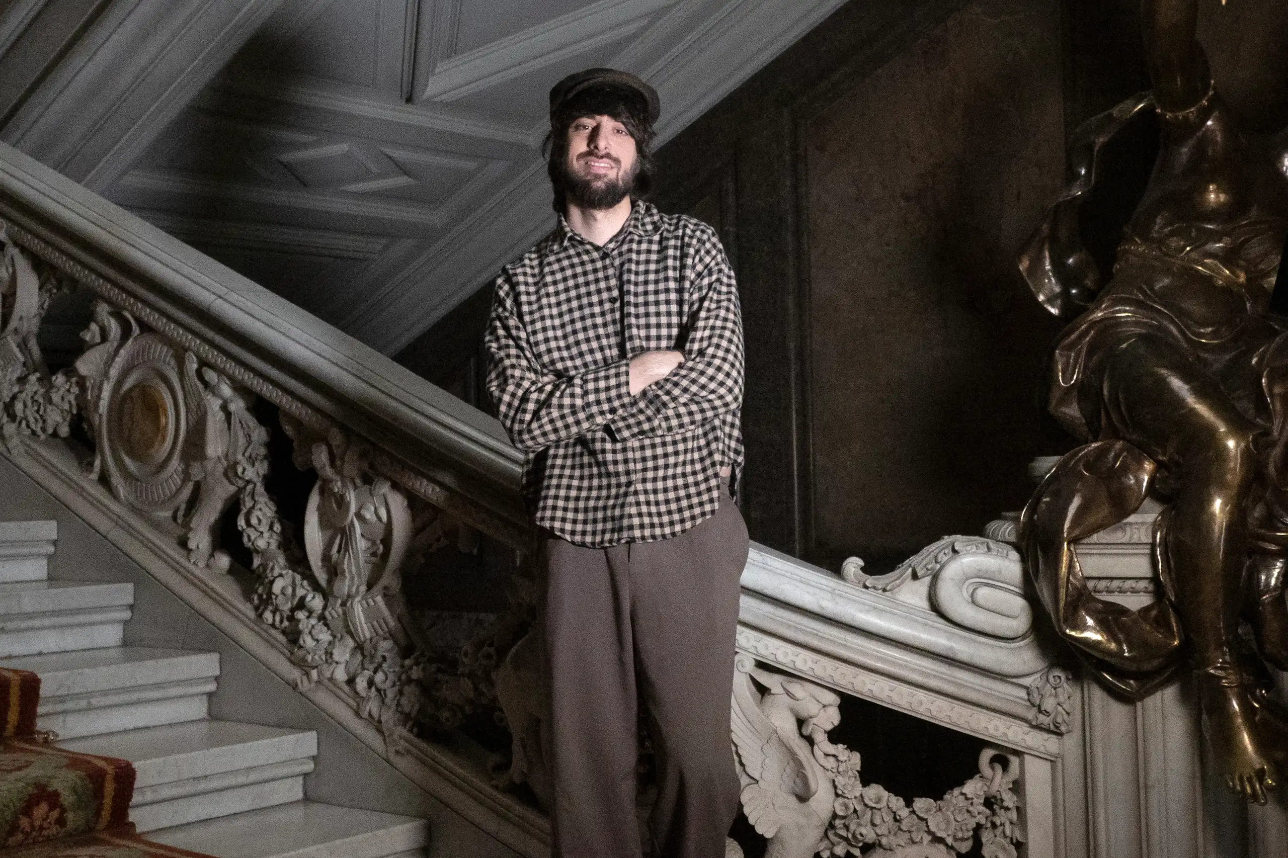 Un hombre alto y con boina posa en una escalera.