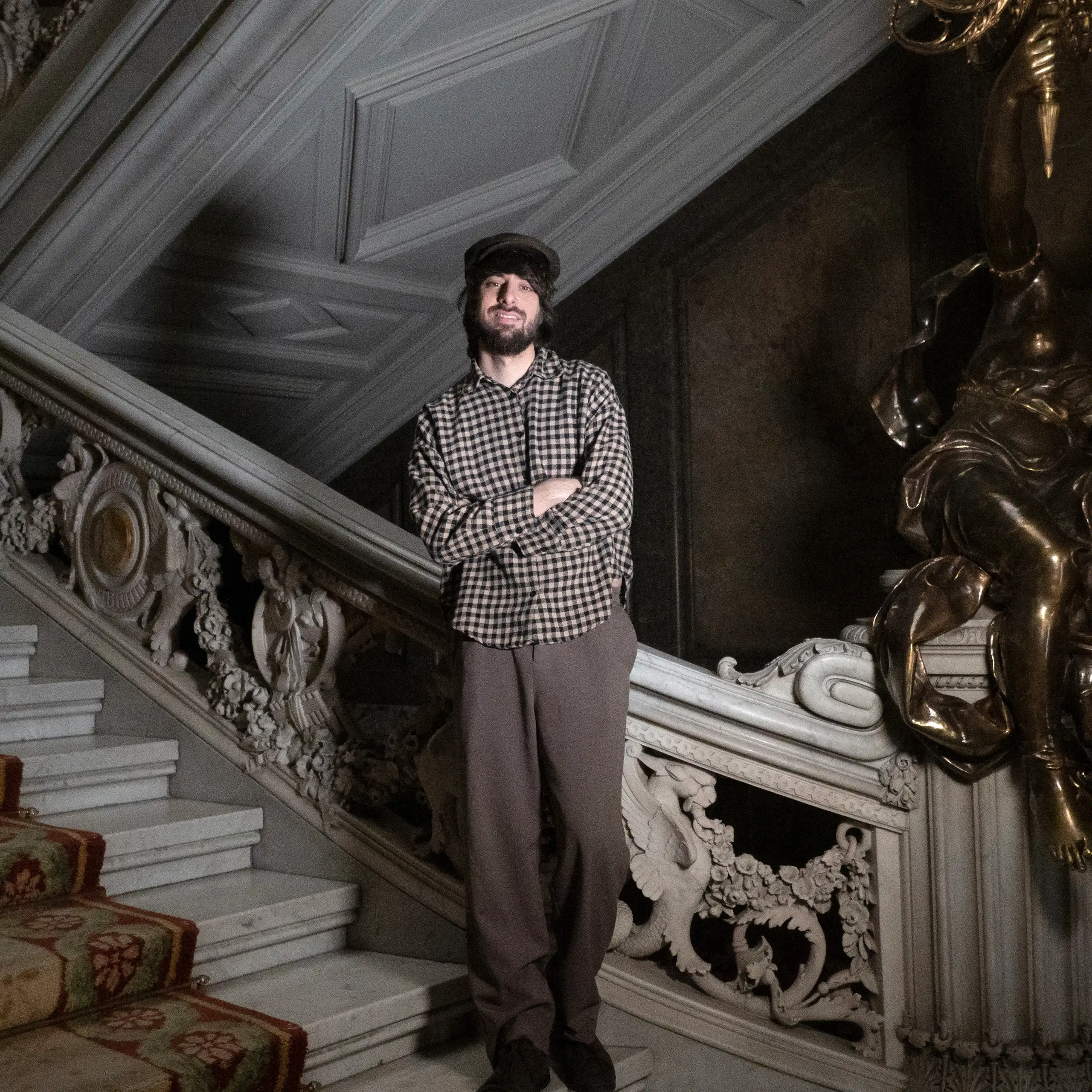 Un hombre alto y con boina posa en una escalera.