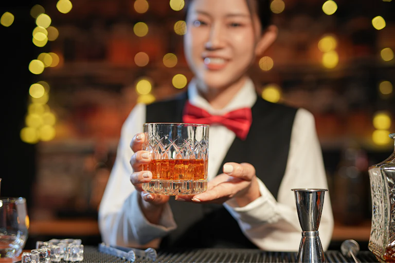 young chinese bar worker holds out a crystal glass of whisky
