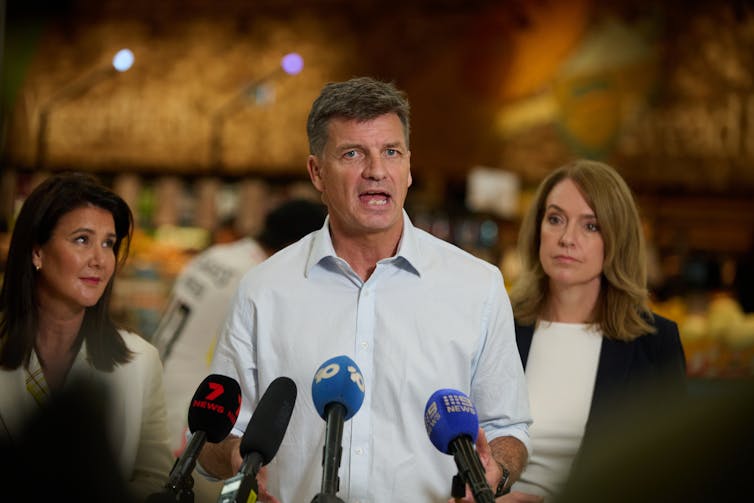 A man stands in front of a supermarket and addresses the media