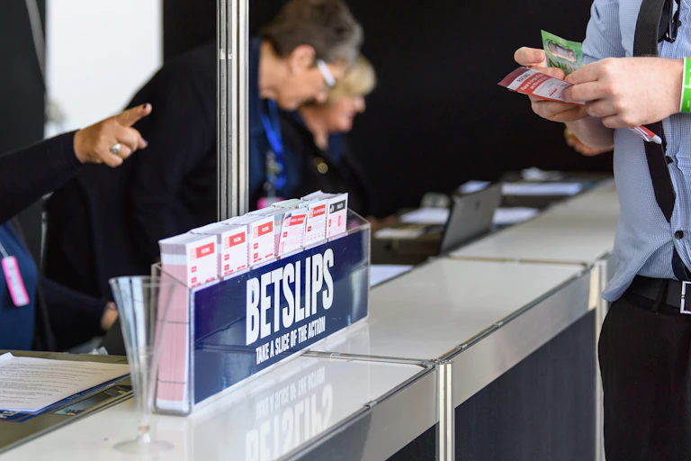 A container of betting slips on a bookmaker's counter, with someone nearby preparing to make a bet