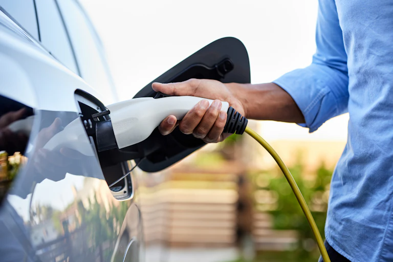 man's hand inserting EV charger plug into car.