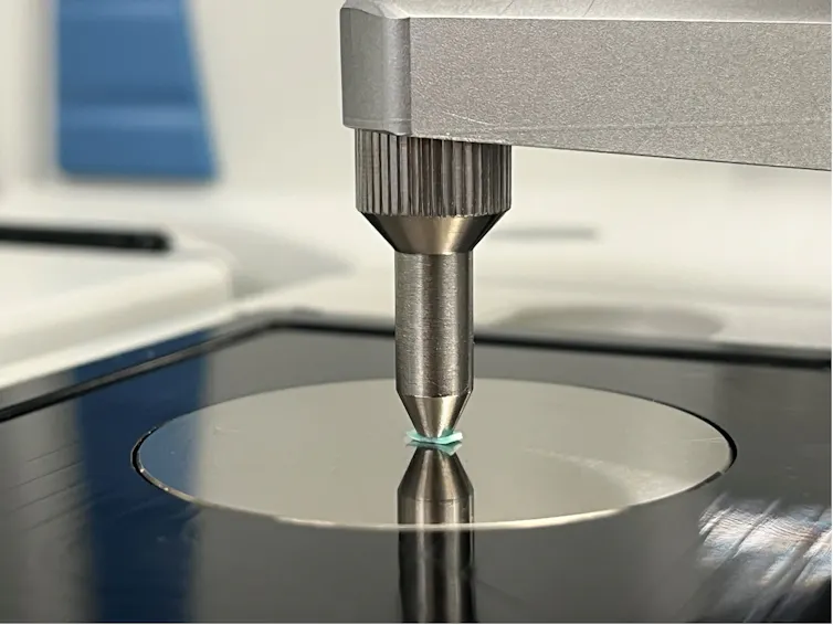 Close-up of a steel instrument with a probe placed on a small piece of green plastic.