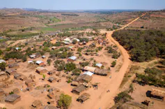 A village seen from the sky, with less than 100 houses on dry red sand and a few bushes here and there