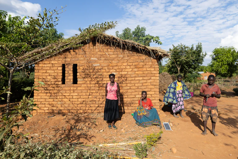 Four people outside a rural home with a tiny solar panel about A4 size