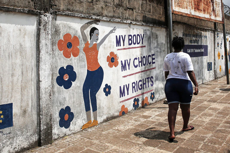 An African woman walks down a street past a mural that reads "My body. My rights. My choice."