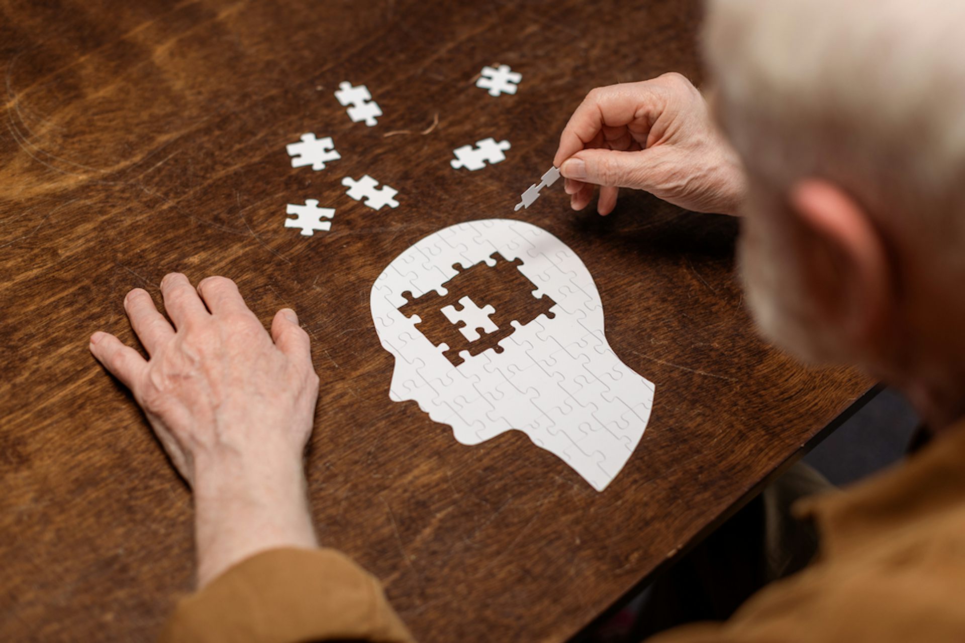 Elderly man doing a puzzle shaped like a human head.