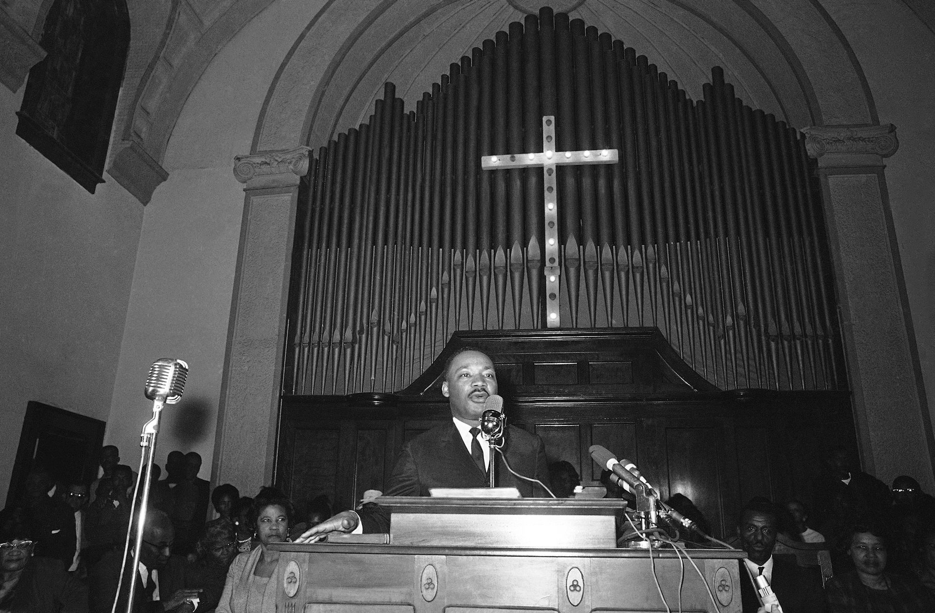 Martin Luther King stands at the pulpit of a church in front of a large crucifix.