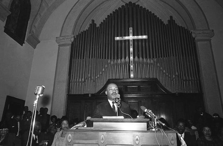 Martin Luther King stands at the pulpit of a church in front of a large crucifix.