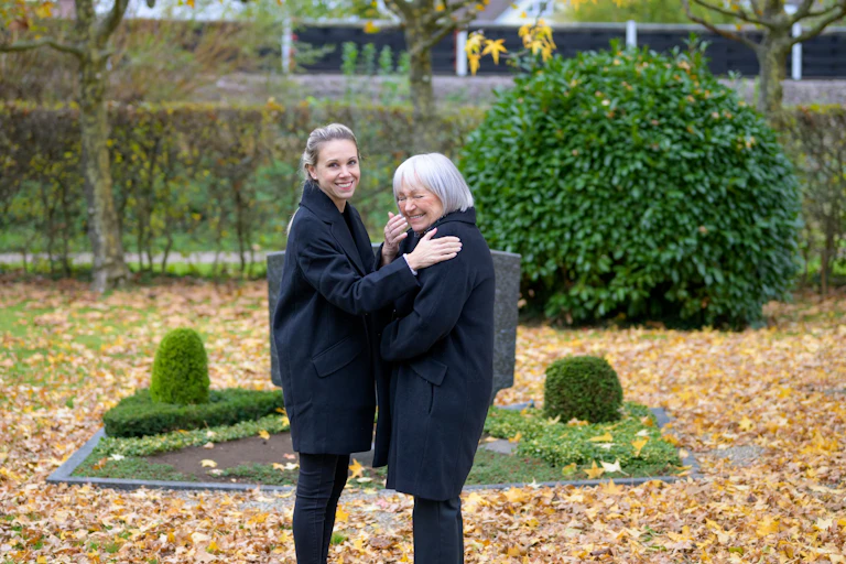 Two women laughing in front of a tombstone.