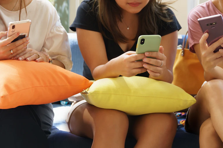 Three girls sitting together on a couch looking at their smartphones