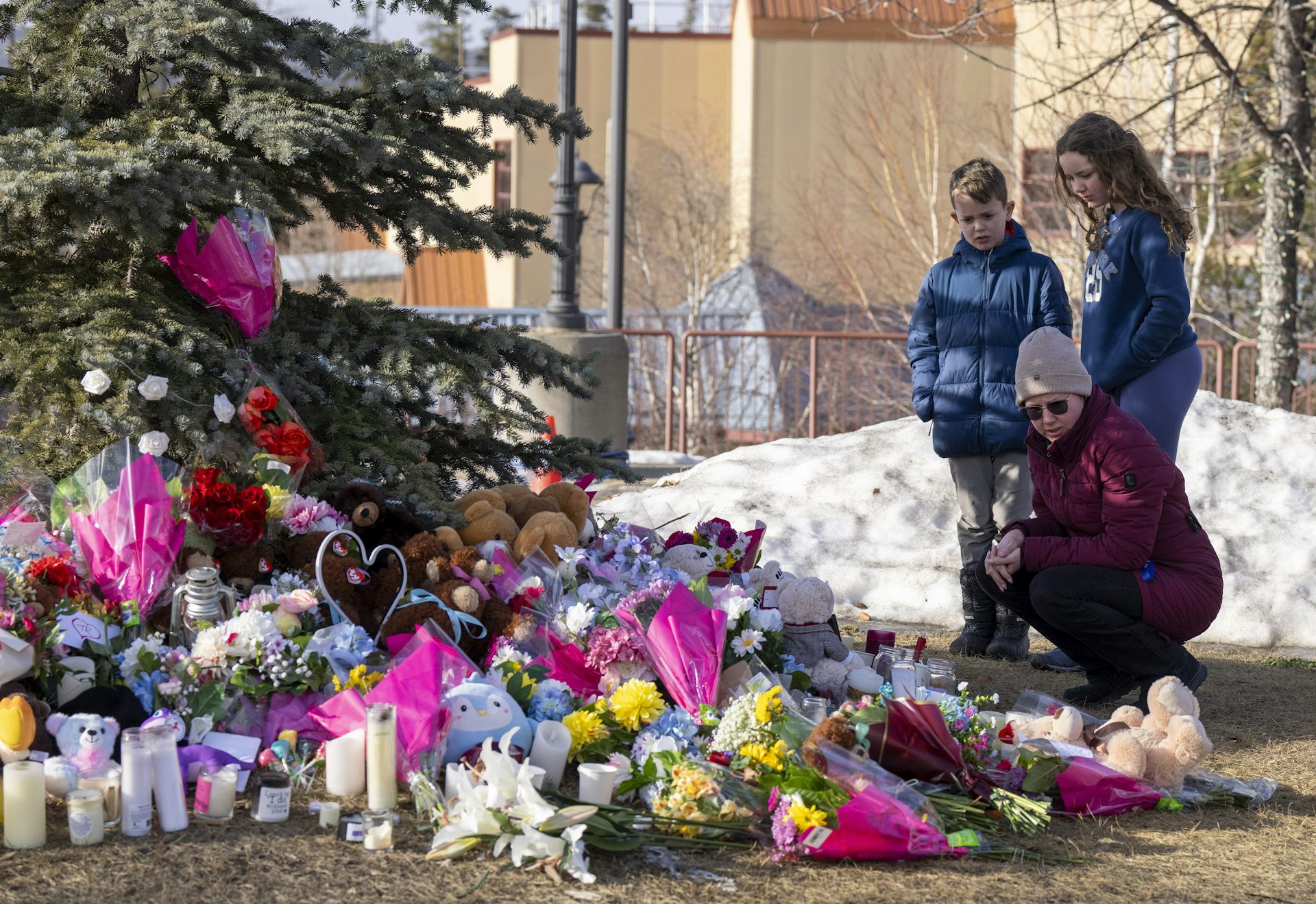 Una mujer y dos niños están junto a un monumento conmemorativo hecho de flores.