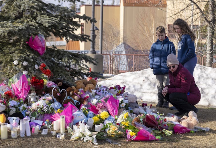 Una mujer y dos niños están junto a un monumento conmemorativo hecho de flores.