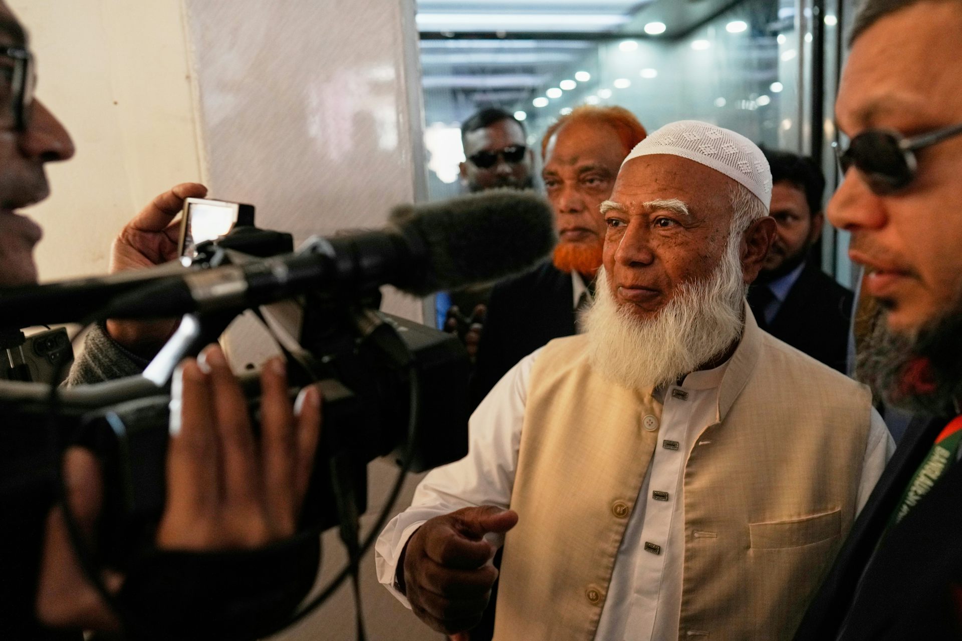 Un anciano de barba blanca habla con periodistas con cámaras.