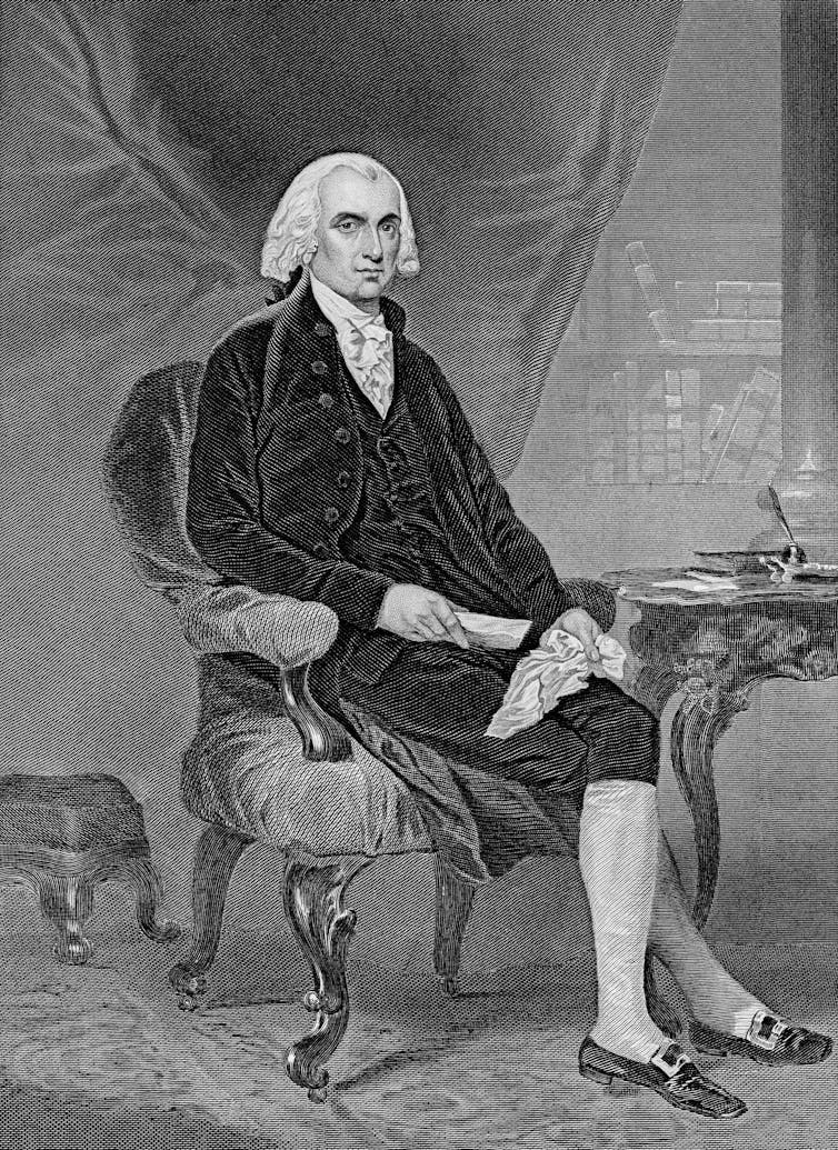 Lo que James Madison puede enseñar a los estadounidenses sobre la libertad religiosa actual 1 Un hombre majestuoso con peluca blanca, chaleco negro y pantalones hasta las rodillas está sentado con las piernas cruzadas junto a una mesa de madera.
