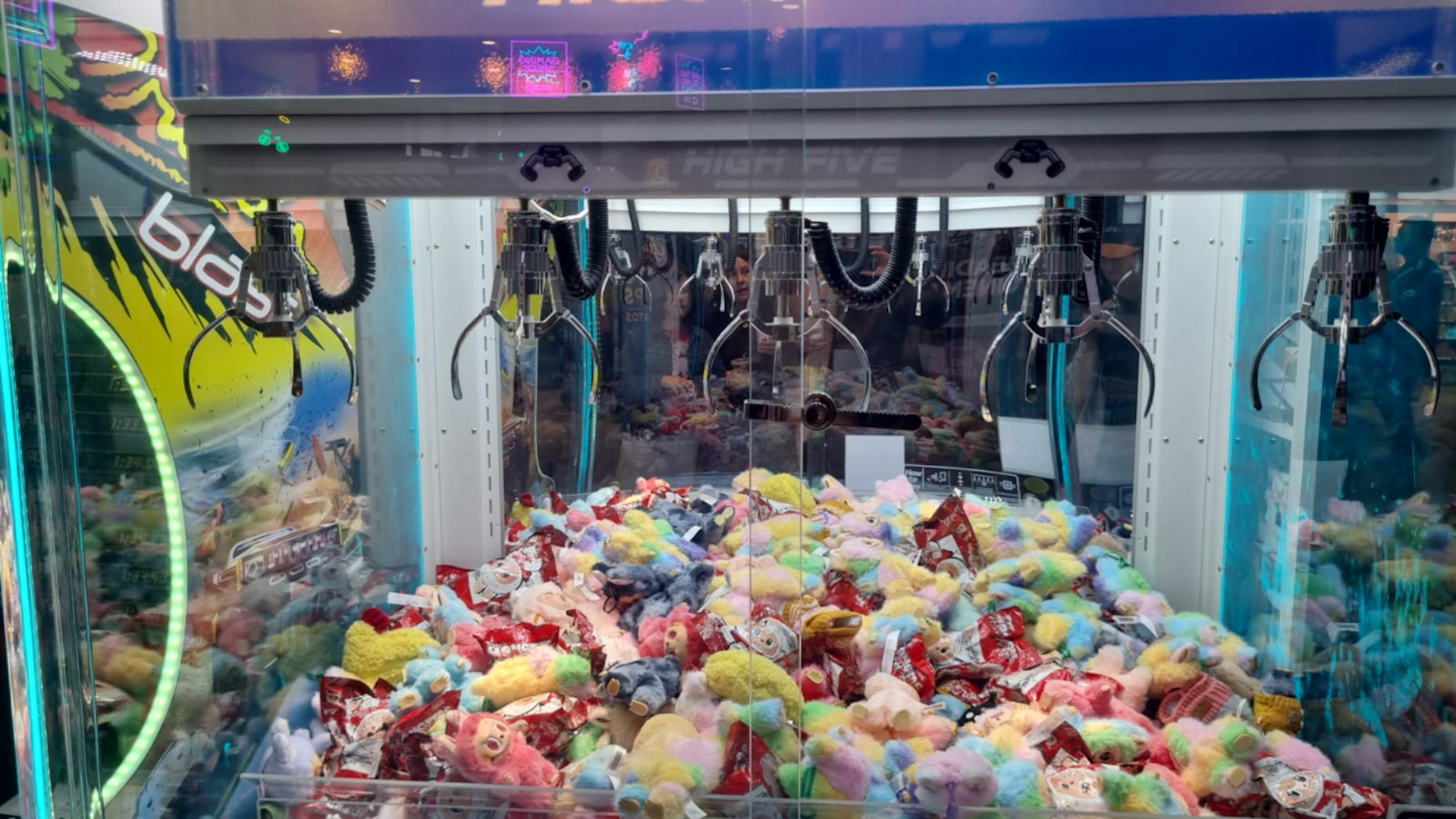 Close-up view of a claw machine with several claws, filled with a wide variety of colourful toys.