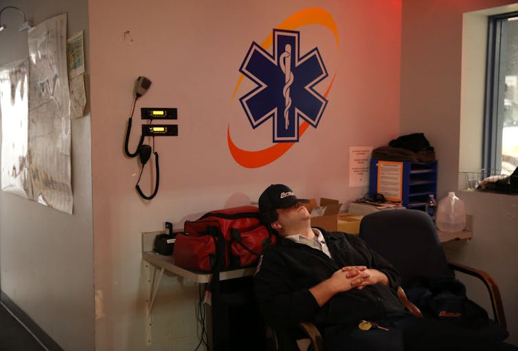 An emergency services technician with a hat covering his face is seen napping in a station break room.