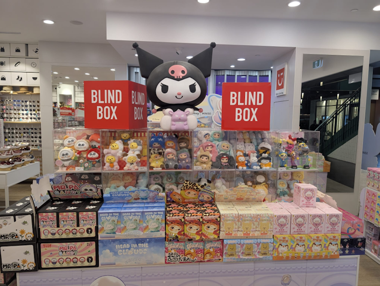 Several rows of toys and blind boxes are on display in a shop. Two large red cubes read 'blind box'.