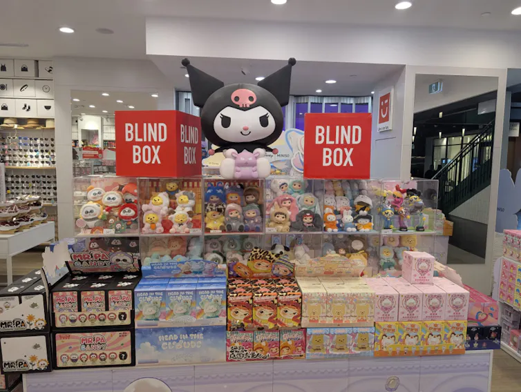 Several rows of toys and blind boxes are on display in a shop. Two large red cubes read 'blind box'.