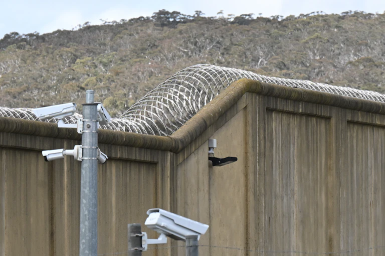 A high concrete wall with barbed wire and security cameras facing in multiple directions