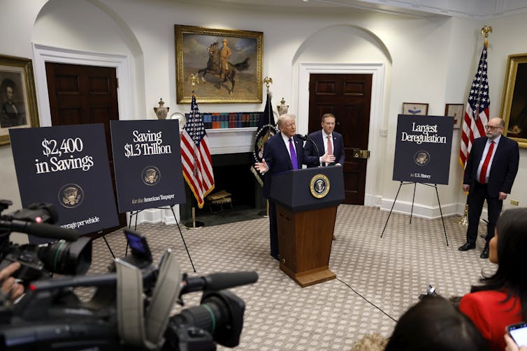 us president donald trump at a lectern at the white house with posters saying $2,400 in savings and saving $1.3 trillion