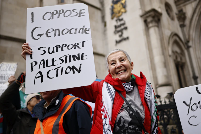 Palestine Action supporters outside the royal courts of justice, carrying placards that read 'I oppose genocide I support Palestine Action' and 'up yours Cooper'