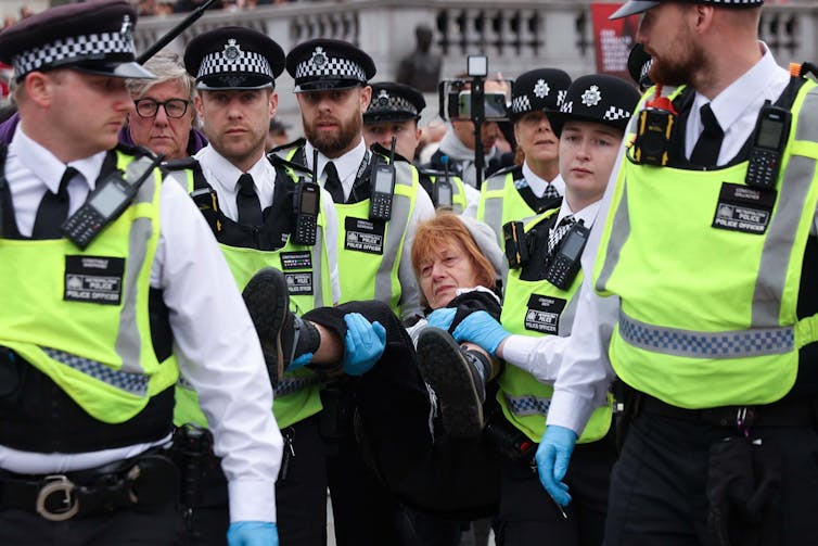 A group of Met Police carrying an older female protester in an arrest