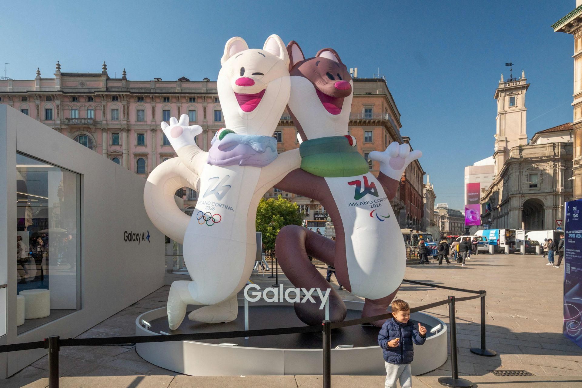 Two mascots of the Milano Cortina Winter Olympic Games in a town square