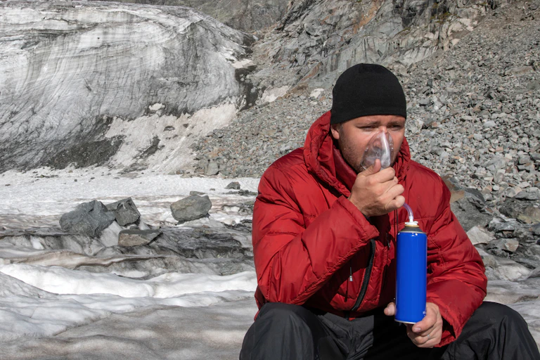 Mountaineer breathing oxygen in front of a glacier covered with snow and ice.