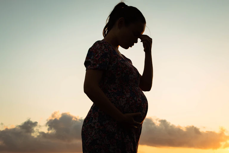 Silhouetted image of pregnant woman holding her hands to her forehead