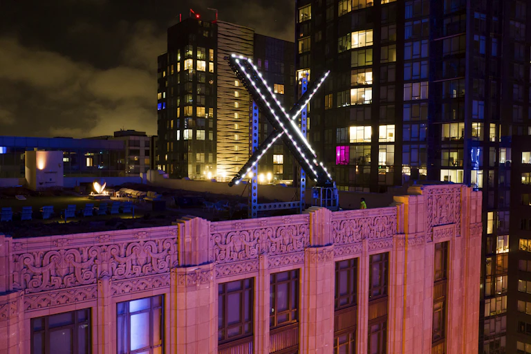 A stone building lit with pink lights, with a large X on the roof.