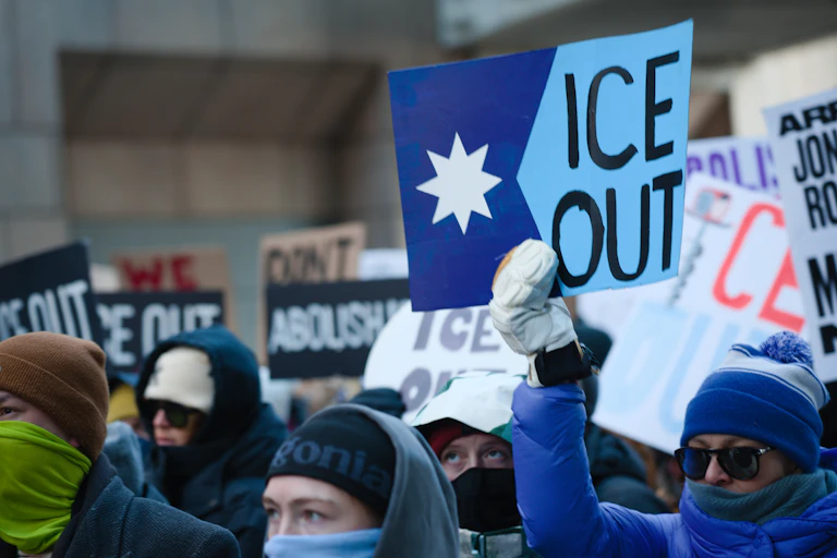 People in winter hats hold signs protesting against ICE in Minneapolis.