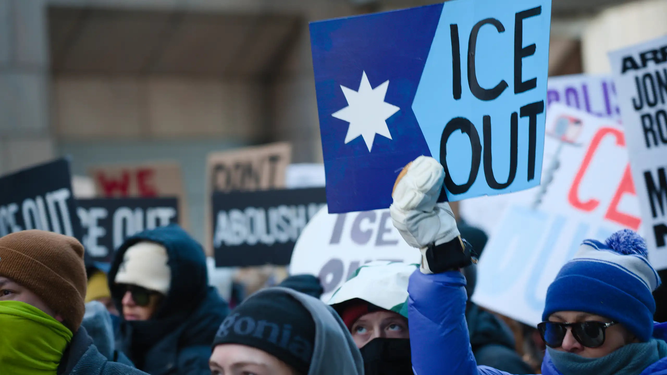 People in winter hats hold signs protesting against ICE in Minneapolis.
