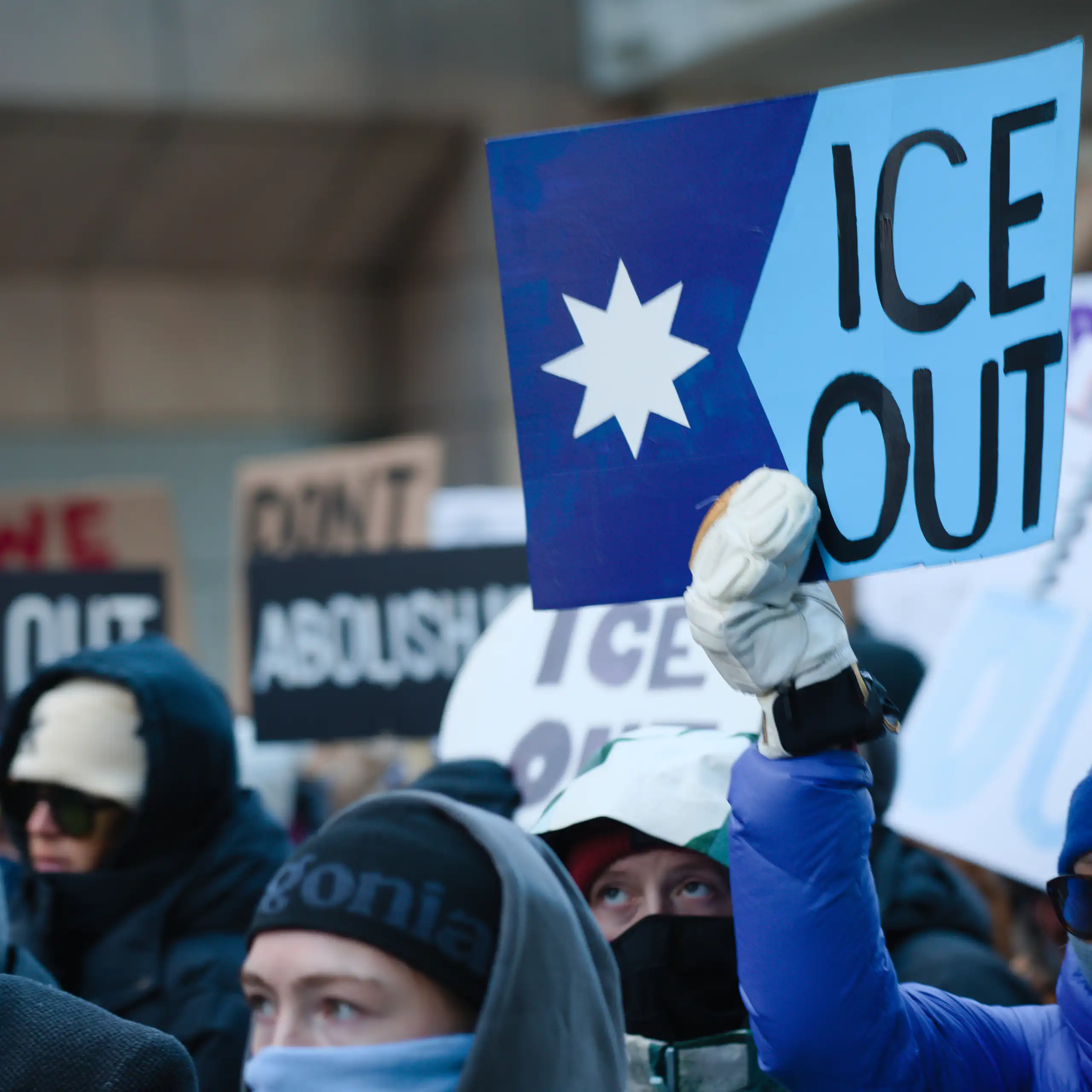 People in winter hats hold signs protesting against ICE in Minneapolis.