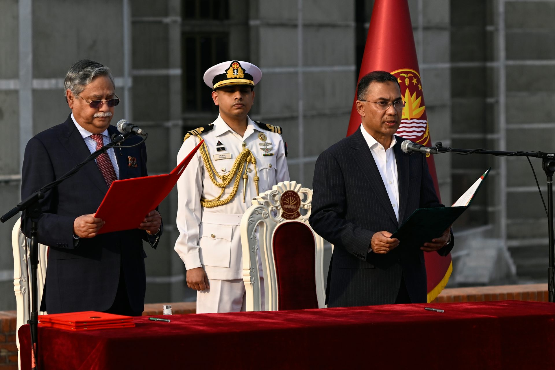 two men stand behind a table with open binders in their hands. A soldier in a white uniform stands behind them