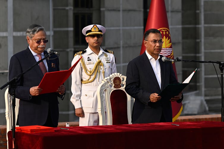 two men stand behind a table with open binders in their hands. A soldier in a white uniform stands behind them