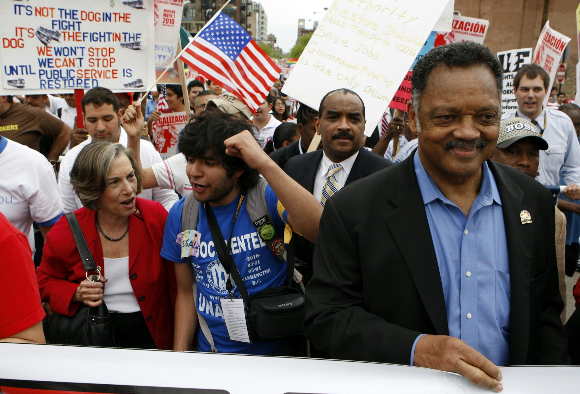 Jesse Jackson smiles bemusedly, holding a sign as he stands in front of other marchers.