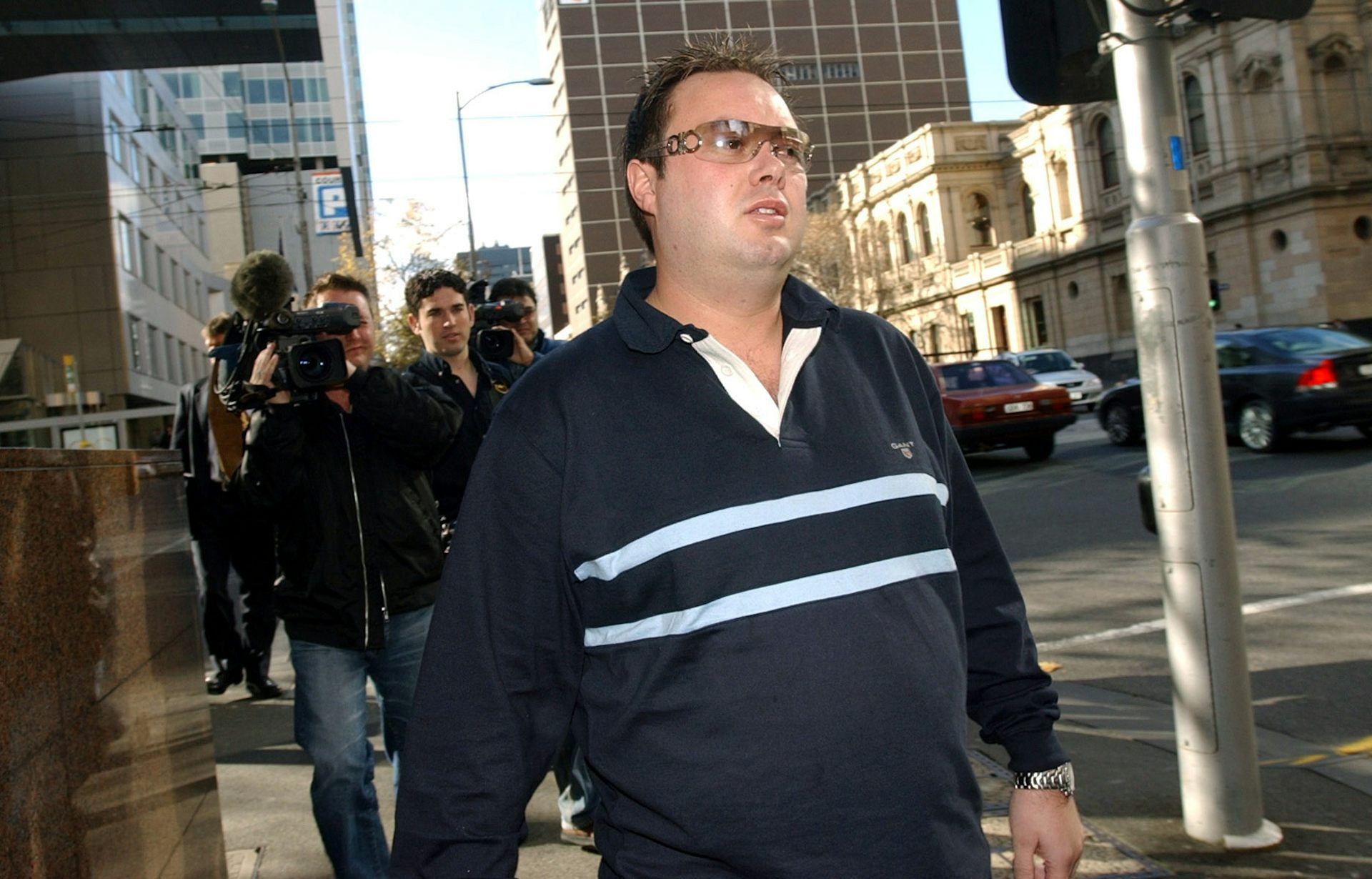 A man with rimless sunglasses walks down a city street
