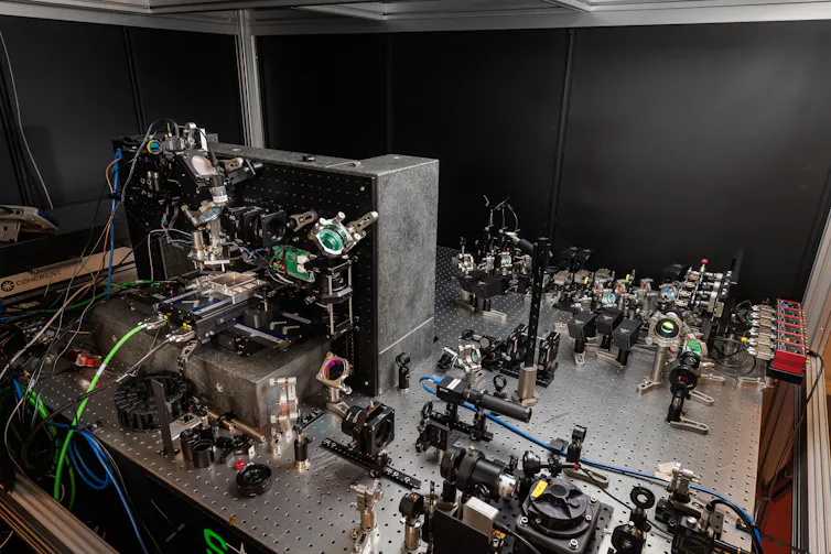 Photo of a lab bench covered in lasers and lenses.
