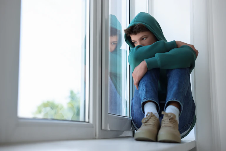 Chico con además triste sentado junto a una ventana.