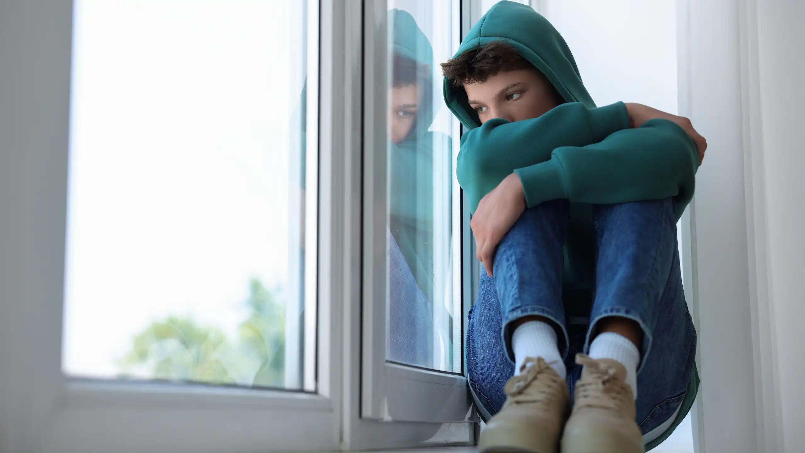 Chico con además triste sentado junto a una ventana.