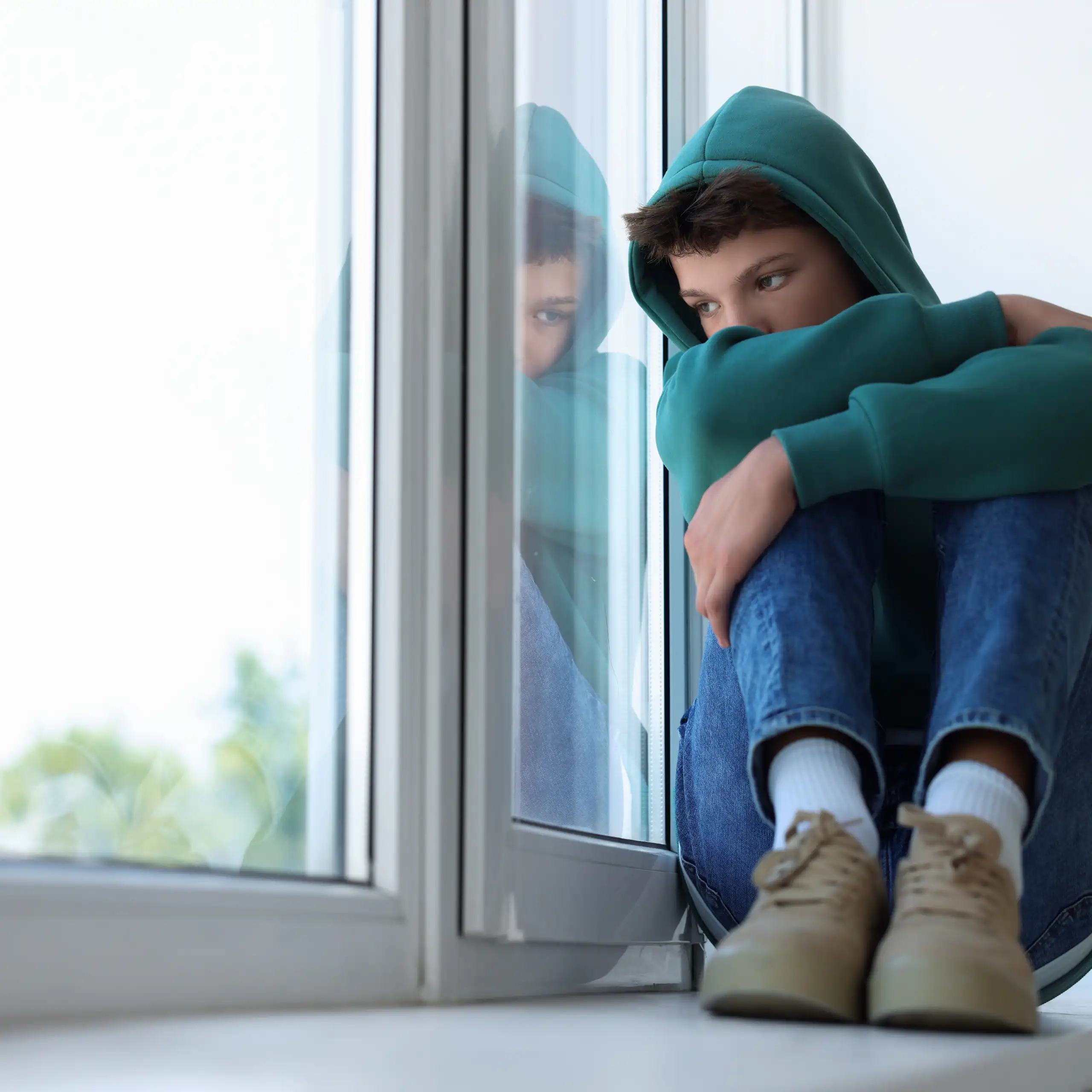 Chico con además triste sentado junto a una ventana.
