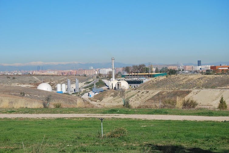 Un paisaje verde con montículos y una infraestructura con chimeneas para la gestión de residuos