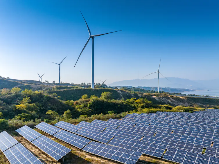 wind and solar farms side by side against a blue sky and mountains in the distance.